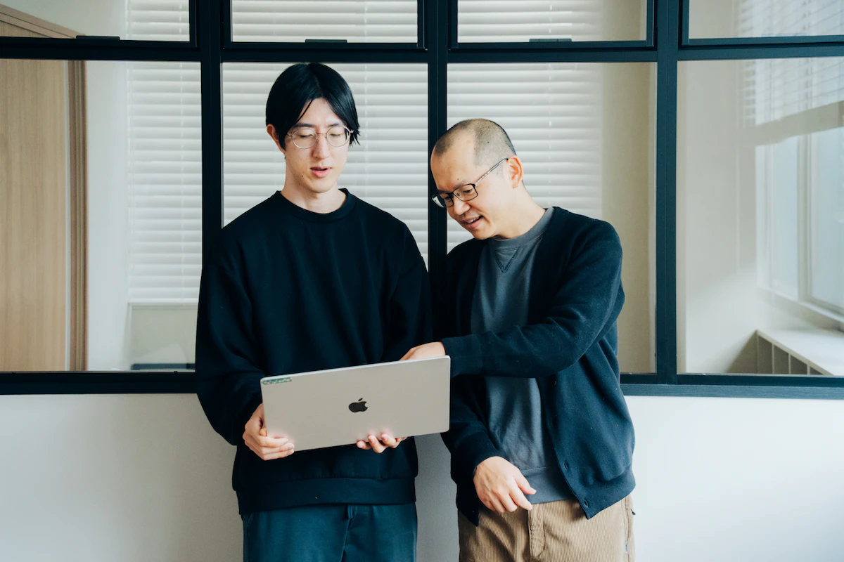 ノートパソコンの画面を指差して話す2人のプログラマ