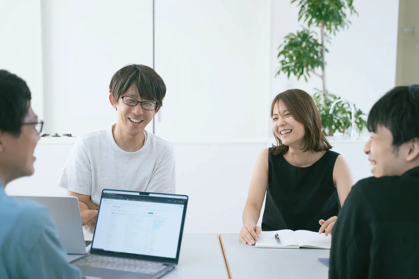 明るい会議室でノートパソコンを囲んで笑顔で打ち合わせをするメンバー